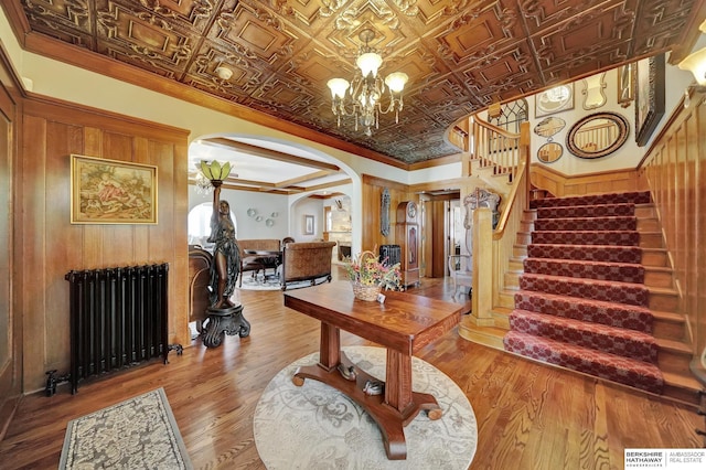 interior space featuring crown molding, radiator heating unit, wooden walls, a notable chandelier, and wood-type flooring