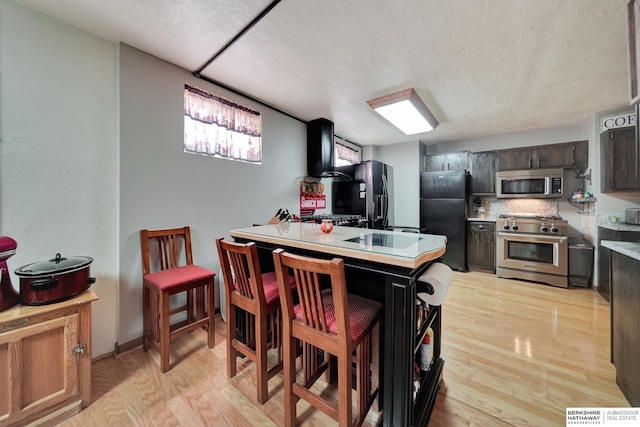 kitchen with a breakfast bar area, light hardwood / wood-style floors, kitchen peninsula, stainless steel appliances, and dark brown cabinets