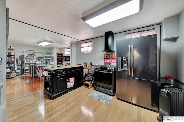 kitchen featuring a textured ceiling, light hardwood / wood-style floors, wall chimney exhaust hood, and appliances with stainless steel finishes