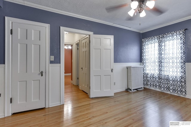 empty room with ceiling fan, ornamental molding, light hardwood / wood-style flooring, and a textured ceiling