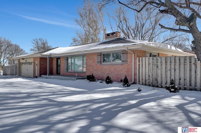 view of front of property with brick siding, a chimney, fence, a garage, and driveway