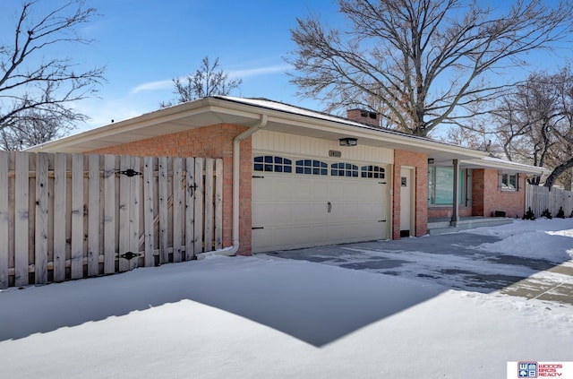 snow covered property featuring a garage, a chimney, fence, and brick siding