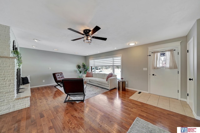 living area with visible vents, baseboards, a ceiling fan, light wood-type flooring, and a brick fireplace