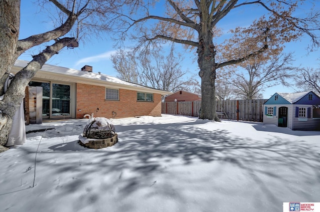 yard layered in snow featuring an outbuilding, an outdoor fire pit, and fence