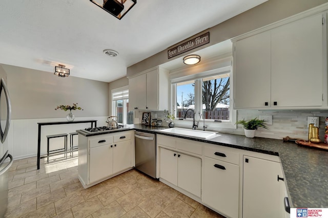 kitchen with white cabinets, dark countertops, a peninsula, stainless steel appliances, and a sink