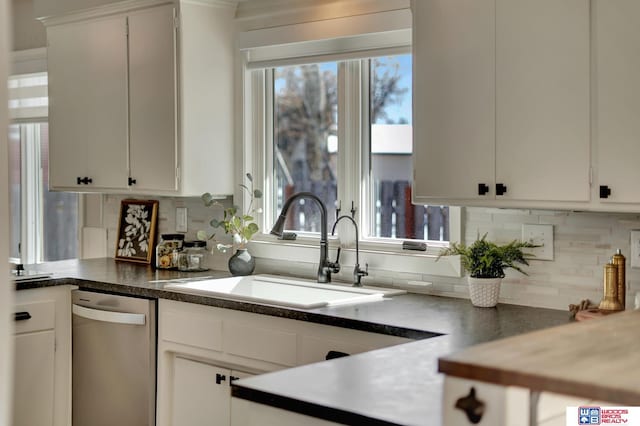 kitchen with dark countertops, dishwasher, white cabinets, and a sink