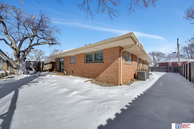 snow covered property with brick siding, fence, and central AC unit