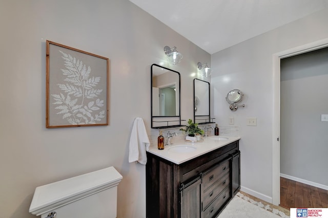 full bath with double vanity, baseboards, a sink, and wood finished floors