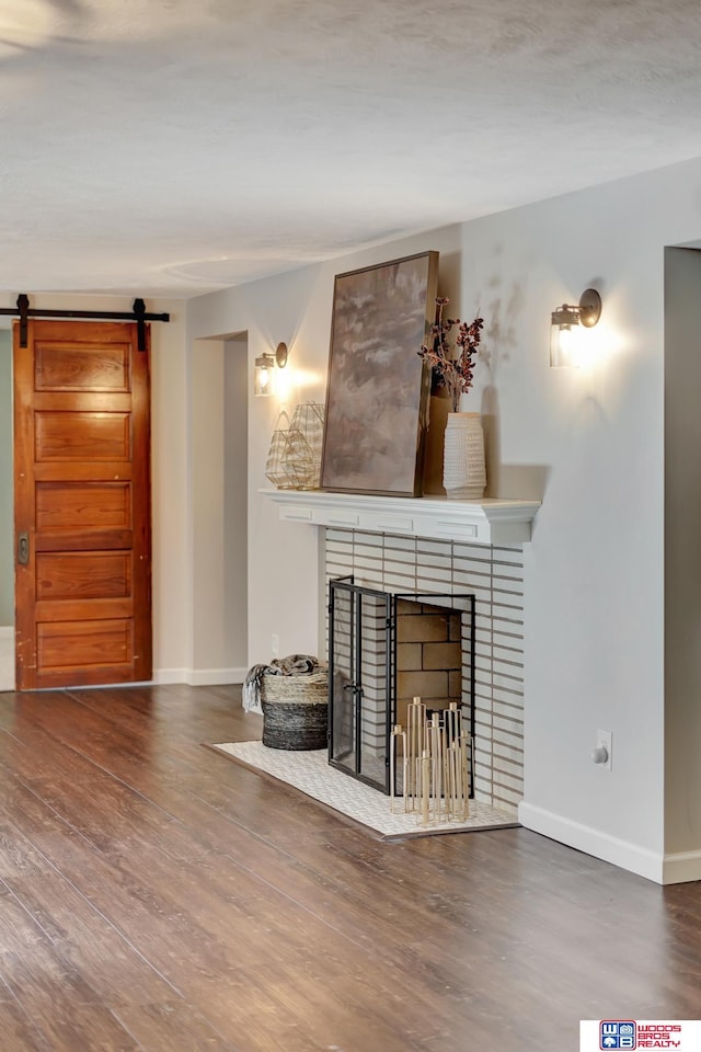 unfurnished living room with wood finished floors, a brick fireplace, baseboards, and a barn door