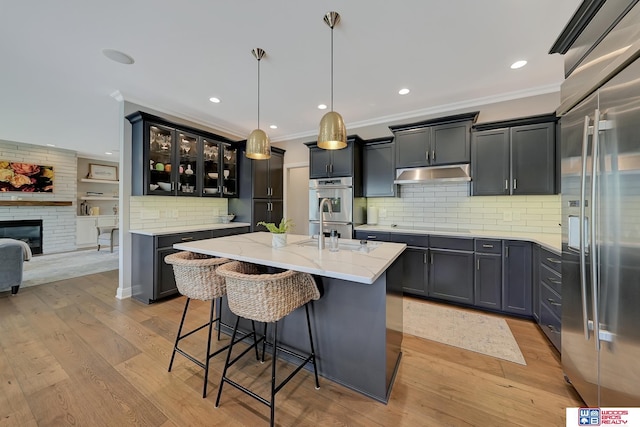 kitchen with appliances with stainless steel finishes, decorative light fixtures, tasteful backsplash, a kitchen island with sink, and light stone countertops