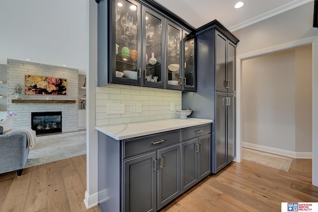 bar with crown molding, light stone counters, a brick fireplace, decorative backsplash, and light wood-type flooring