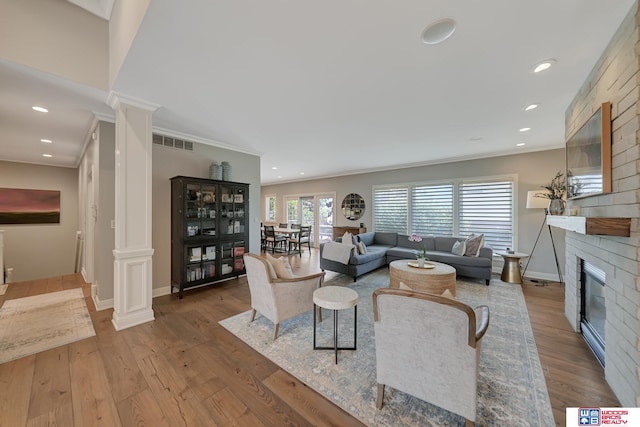 living room featuring crown molding, a fireplace, decorative columns, and hardwood / wood-style flooring