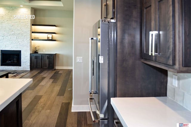 kitchen with stainless steel refrigerator, dark brown cabinetry, wood-type flooring, and a stone fireplace