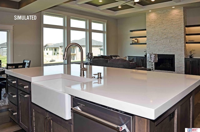 kitchen featuring coffered ceiling, sink, stainless steel dishwasher, a fireplace, and a kitchen island with sink