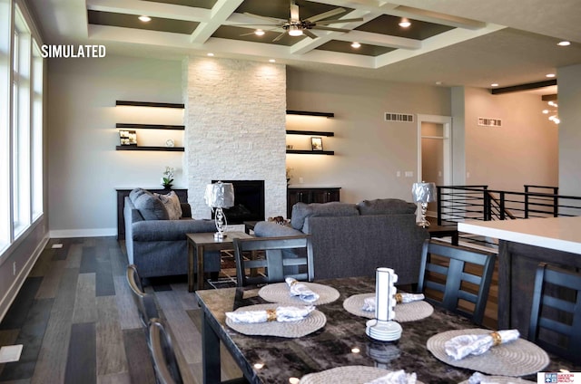 dining area with dark wood-type flooring, ceiling fan, coffered ceiling, a stone fireplace, and beamed ceiling