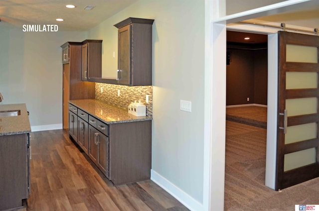 kitchen with dark wood-type flooring, sink, a barn door, light stone countertops, and decorative backsplash