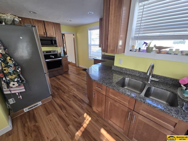 kitchen featuring appliances with stainless steel finishes, dark hardwood / wood-style flooring, sink, and dark stone countertops