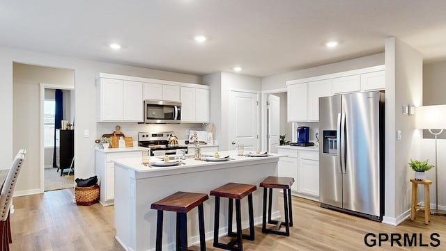 kitchen with appliances with stainless steel finishes, a center island with sink, white cabinets, and light hardwood / wood-style flooring