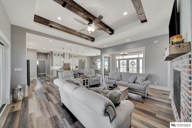 living room featuring beamed ceiling, ceiling fan, a fireplace, and dark wood-type flooring