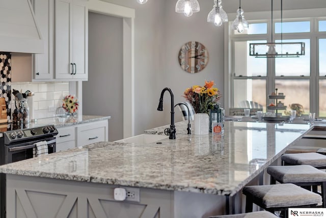 kitchen with white cabinetry, decorative backsplash, custom exhaust hood, hanging light fixtures, and light stone counters