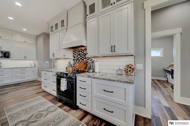 kitchen featuring premium range hood, built in microwave, white cabinetry, light stone counters, and black range with electric cooktop