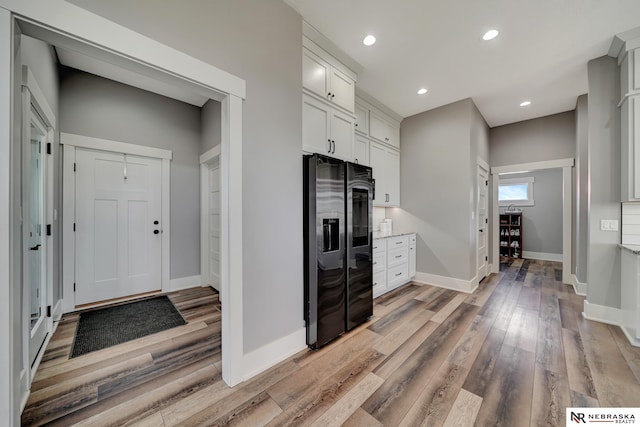 kitchen with black refrigerator with ice dispenser, light hardwood / wood-style floors, and white cabinets