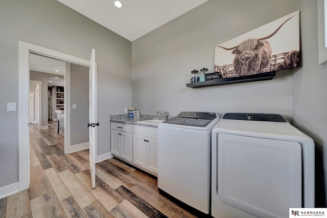 washroom featuring cabinets, sink, washer and clothes dryer, and light hardwood / wood-style flooring