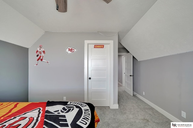 bedroom featuring ceiling fan, light colored carpet, vaulted ceiling, and a textured ceiling