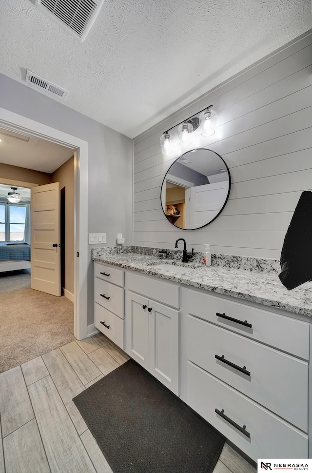 bathroom featuring vanity, wooden walls, and a textured ceiling