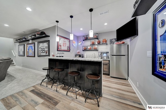 bar with sink, stainless steel fridge, hanging light fixtures, light hardwood / wood-style floors, and light stone countertops