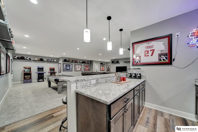 kitchen featuring light stone counters, decorative light fixtures, a kitchen breakfast bar, kitchen peninsula, and light hardwood / wood-style floors