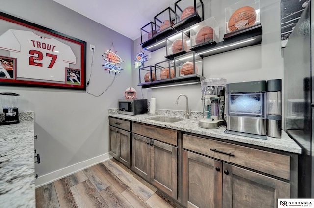 bar with sink, hardwood / wood-style flooring, black refrigerator, dark brown cabinets, and light stone counters