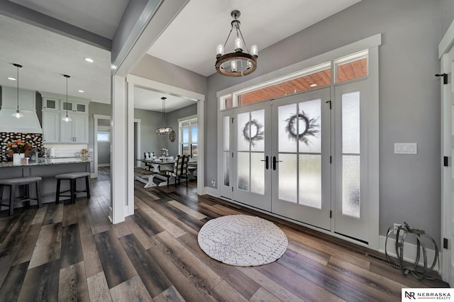 foyer featuring dark wood-type flooring, french doors, and a chandelier