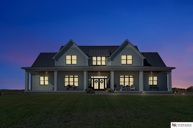 back house at dusk with a porch and a lawn