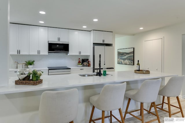 kitchen with sink, a breakfast bar, stove, white cabinetry, and white fridge