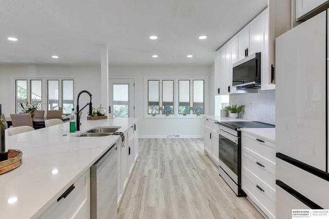 kitchen featuring sink, light stone counters, appliances with stainless steel finishes, light hardwood / wood-style floors, and white cabinets