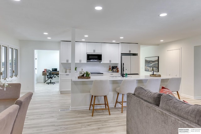 kitchen featuring white fridge, white cabinets, a kitchen bar, and light hardwood / wood-style floors