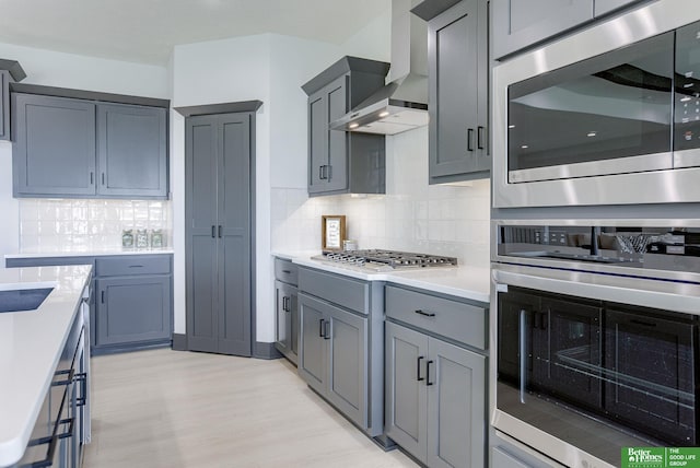 kitchen featuring tasteful backsplash, gray cabinets, wall chimney exhaust hood, and appliances with stainless steel finishes