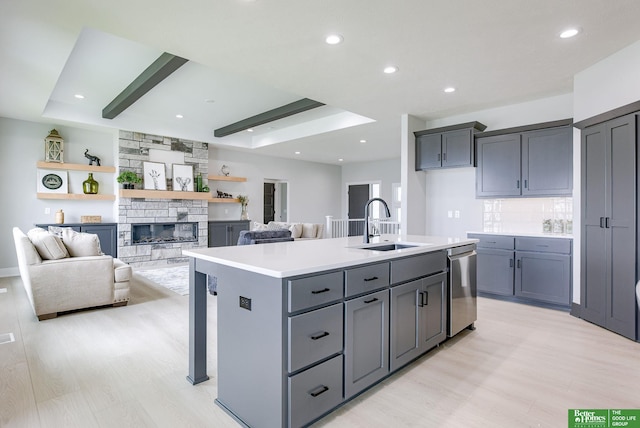 kitchen with sink, gray cabinetry, light hardwood / wood-style floors, an island with sink, and stainless steel dishwasher