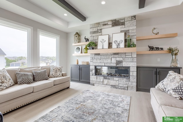 living room with beamed ceiling, a stone fireplace, and light hardwood / wood-style floors