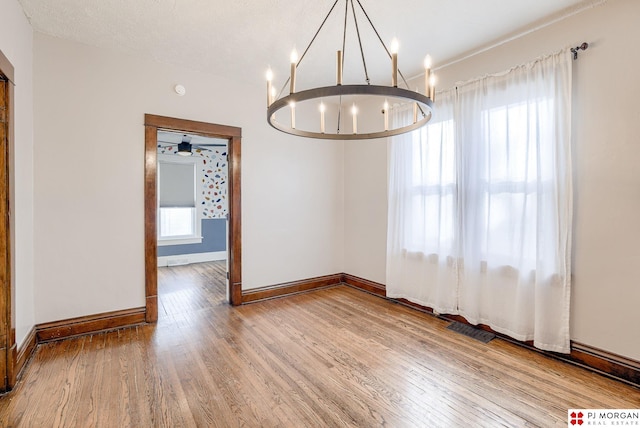 unfurnished dining area featuring an inviting chandelier, wood-type flooring, and a textured ceiling