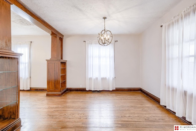 unfurnished dining area featuring an inviting chandelier, light hardwood / wood-style flooring, and a textured ceiling