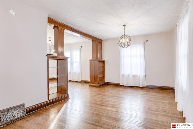 interior space with an inviting chandelier, hardwood / wood-style flooring, a textured ceiling, and ornate columns