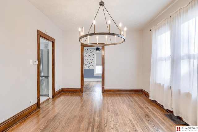 unfurnished dining area featuring plenty of natural light, a chandelier, and wood-type flooring