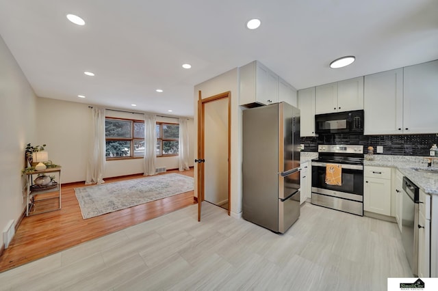 kitchen featuring stainless steel appliances, white cabinets, light stone counters, and light hardwood / wood-style flooring