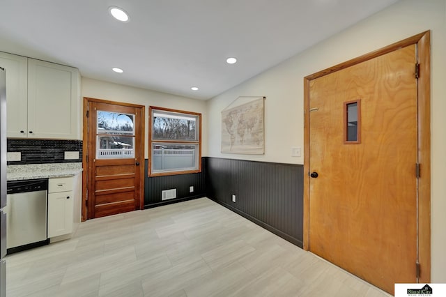 kitchen featuring white cabinetry, light stone countertops, decorative backsplash, and stainless steel dishwasher