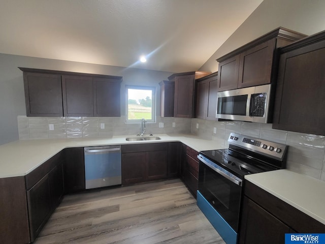 kitchen featuring lofted ceiling, sink, appliances with stainless steel finishes, tasteful backsplash, and light wood-type flooring