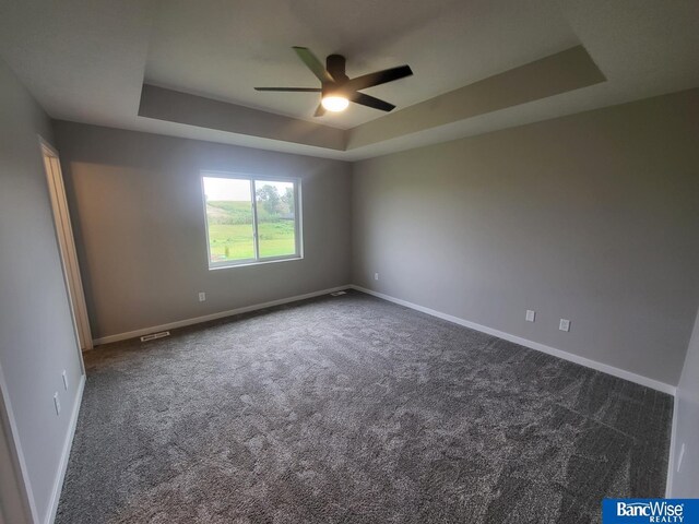 carpeted empty room with ceiling fan and a tray ceiling