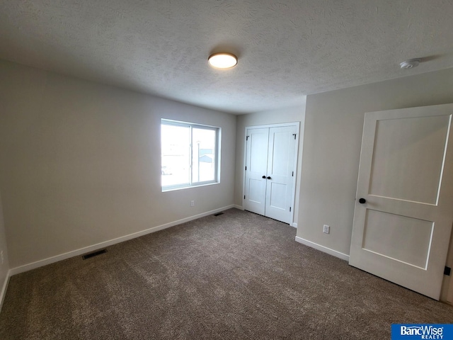 unfurnished bedroom featuring a textured ceiling, carpet flooring, visible vents, baseboards, and a closet