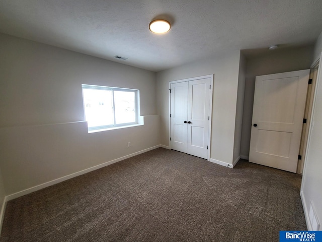 unfurnished bedroom with a closet, a textured ceiling, and dark colored carpet